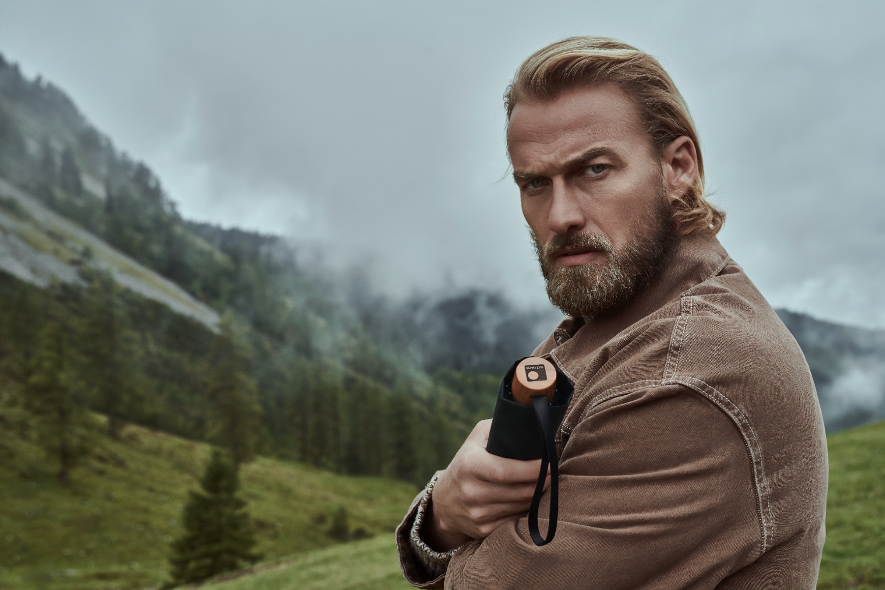 Knirps Timber Regenschirme mit Griffen aus echtem Holz Mann hält geschlossenen Taschenschirm in seiner Hand